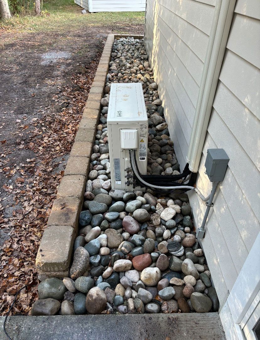 A white box is sitting on top of a pile of rocks next to a house.