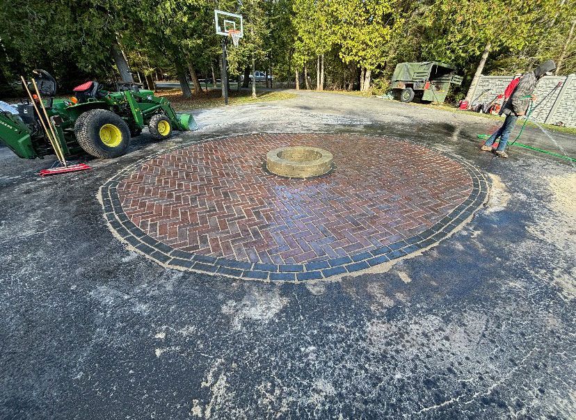A man is cleaning a brick patio with a tractor in the background.