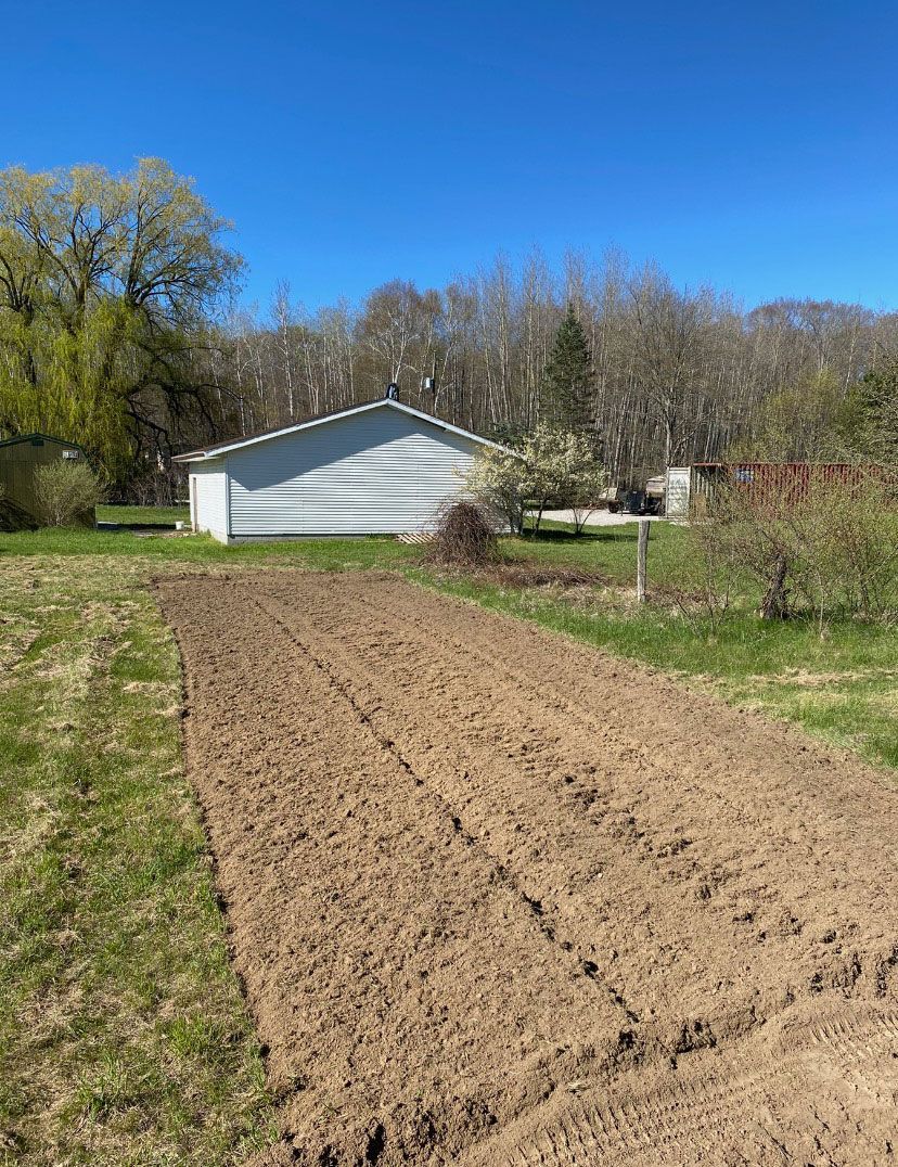 A dirt road leading to a white house in the middle of a field.