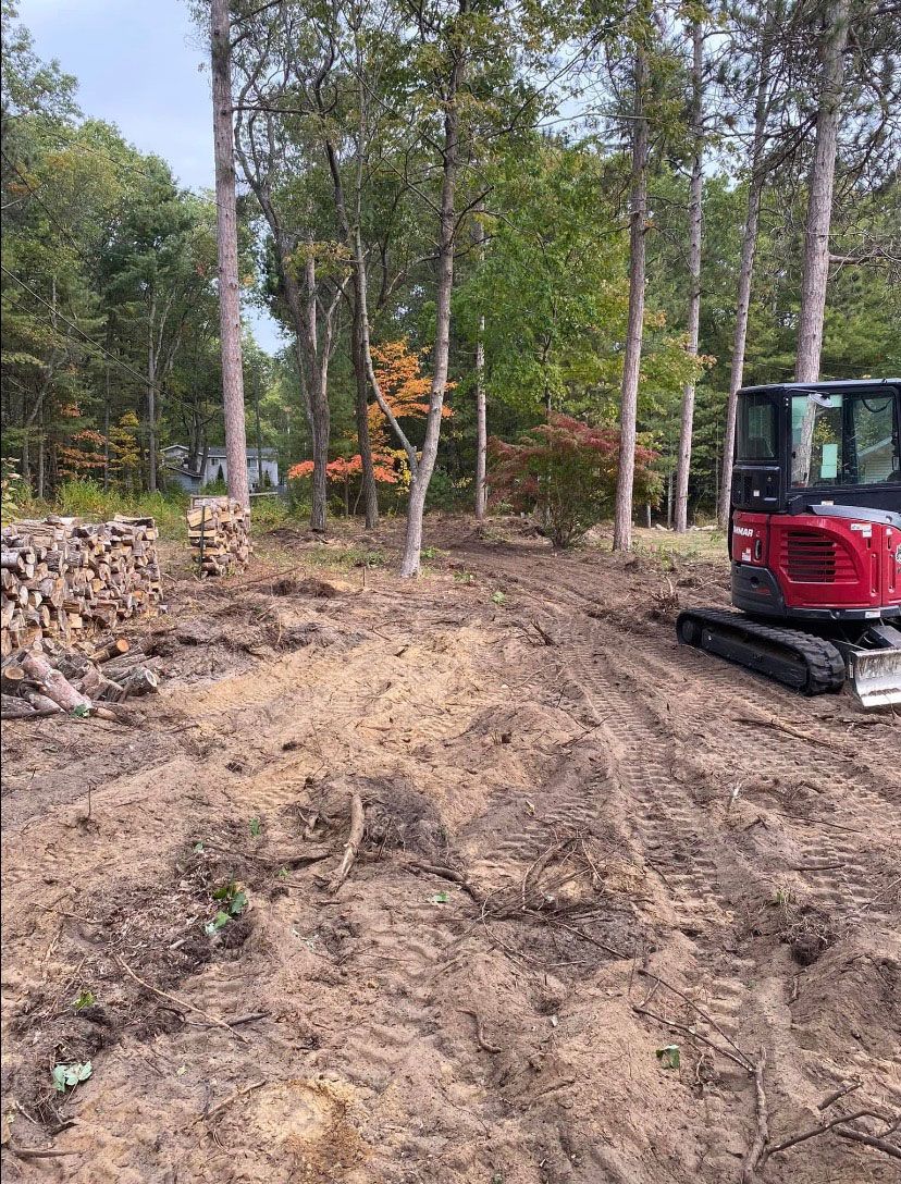 A red bulldozer is driving through a dirt field in the woods.