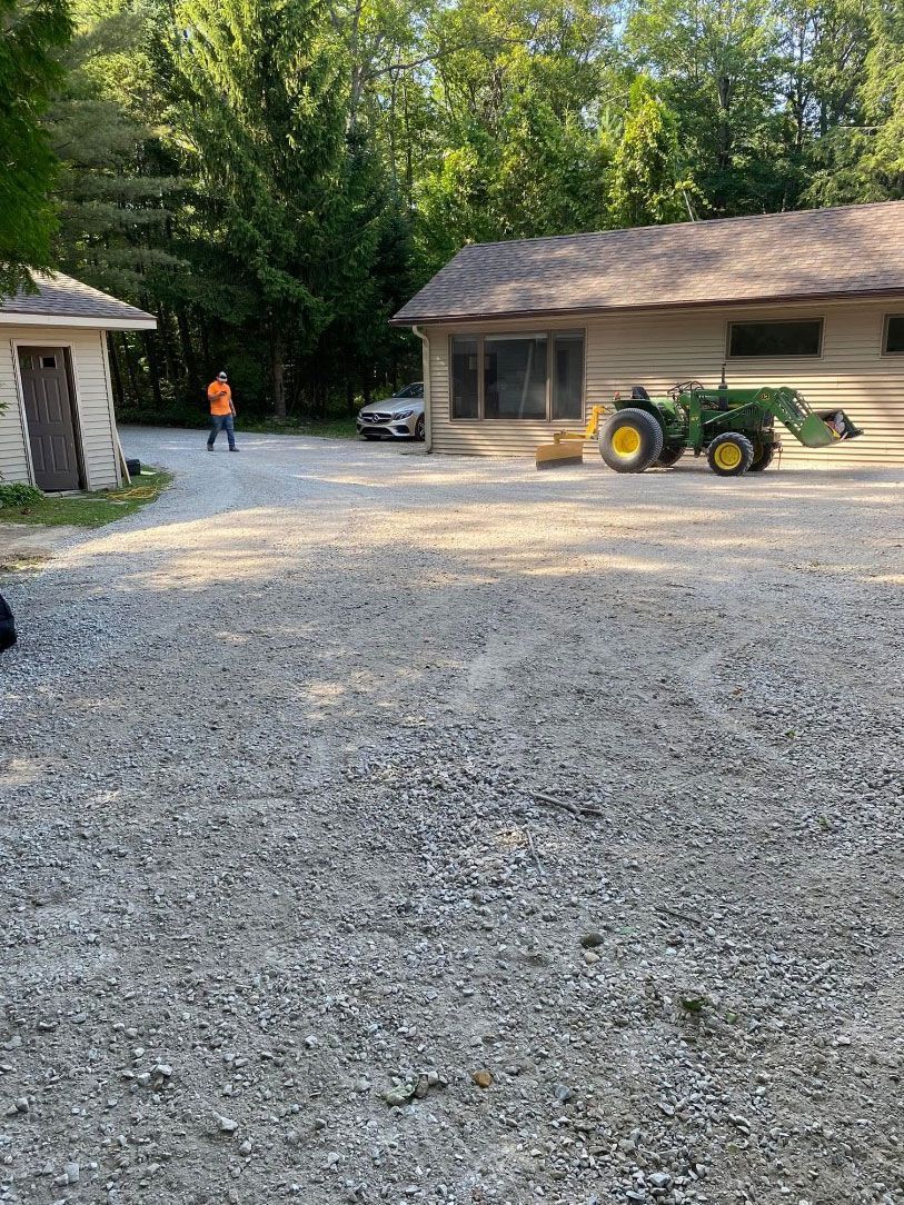 A tractor is parked in a gravel lot in front of a house.