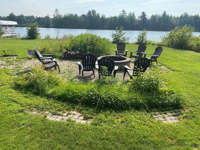 There is a fire pit in the middle of the grass with chairs around it.