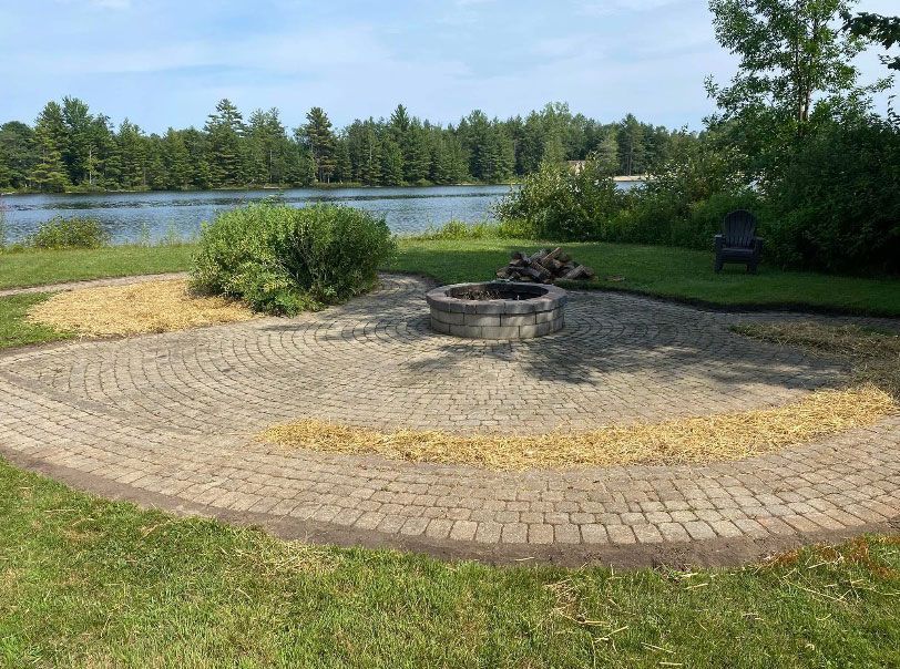 A fire pit is in the middle of a patio next to a lake.