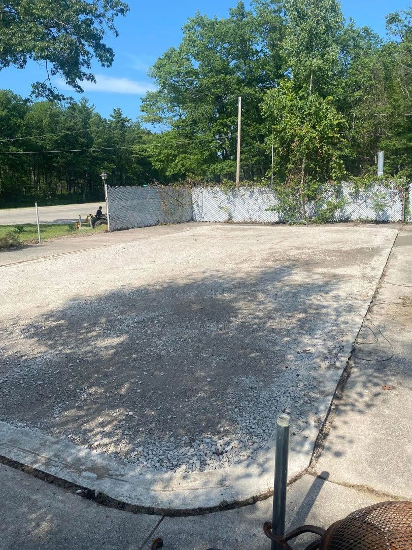 A concrete driveway with a fence and trees in the background.