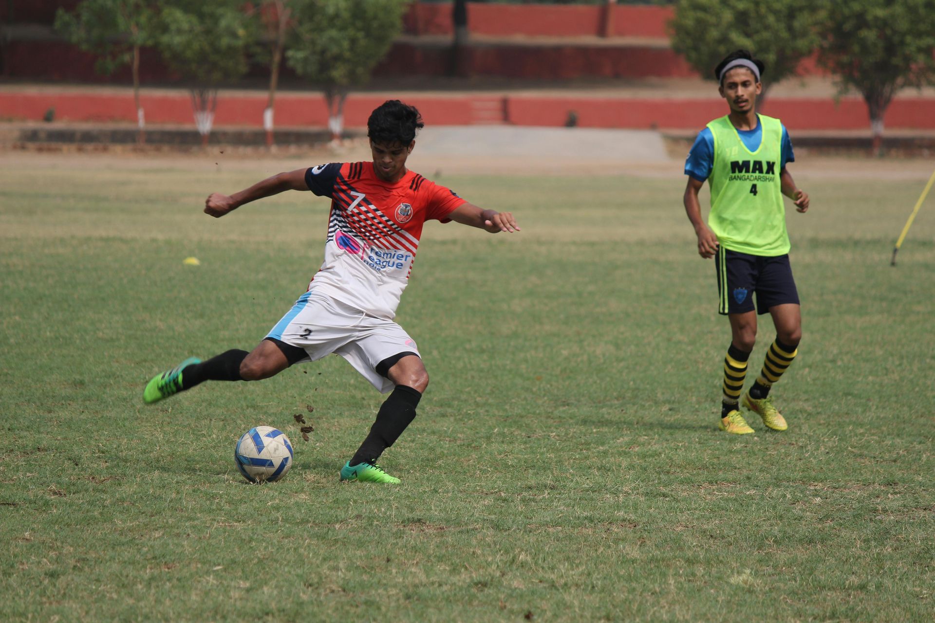A man is kicking a soccer ball on a field while another man watches.