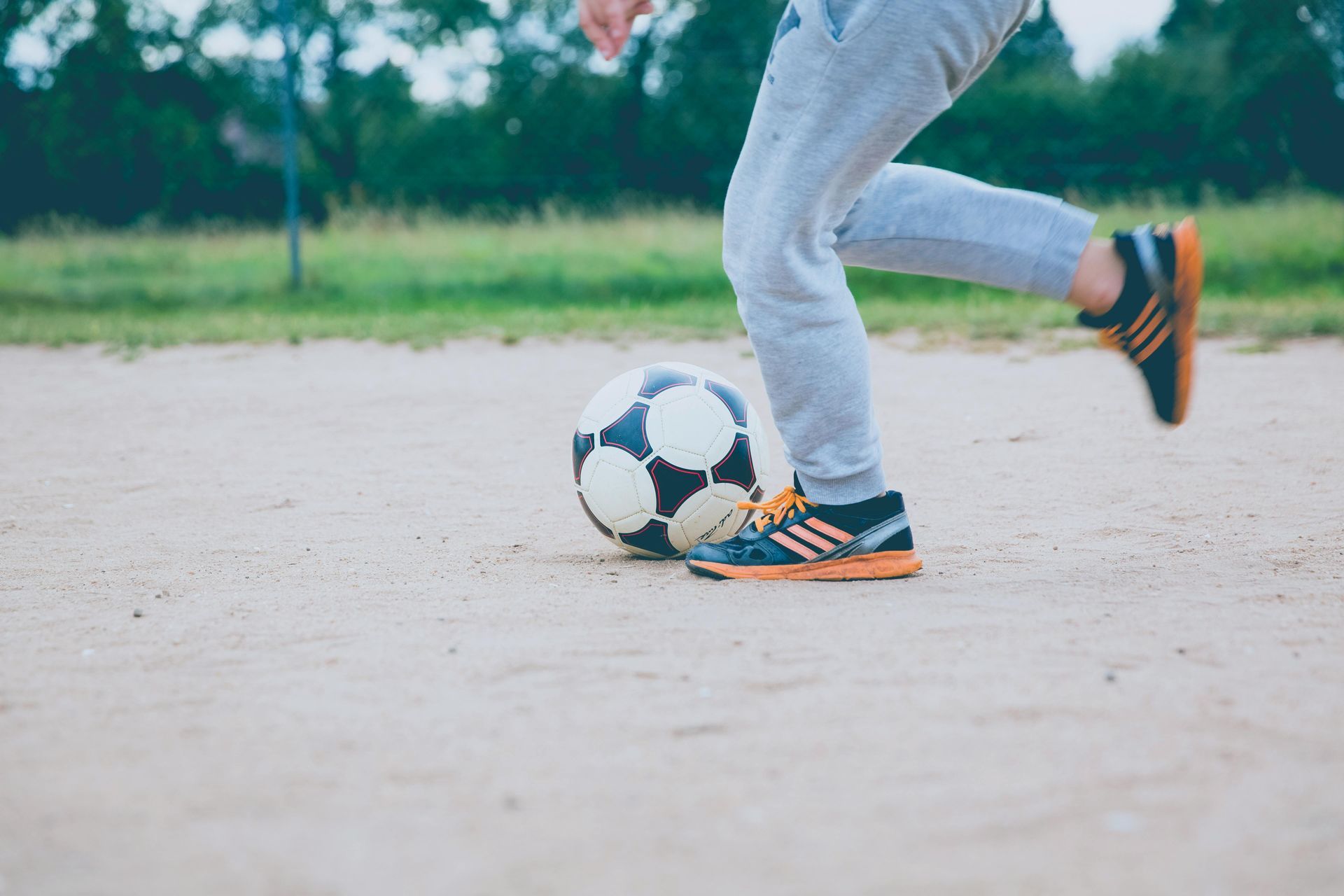 A person is kicking a soccer ball on a dirt field.