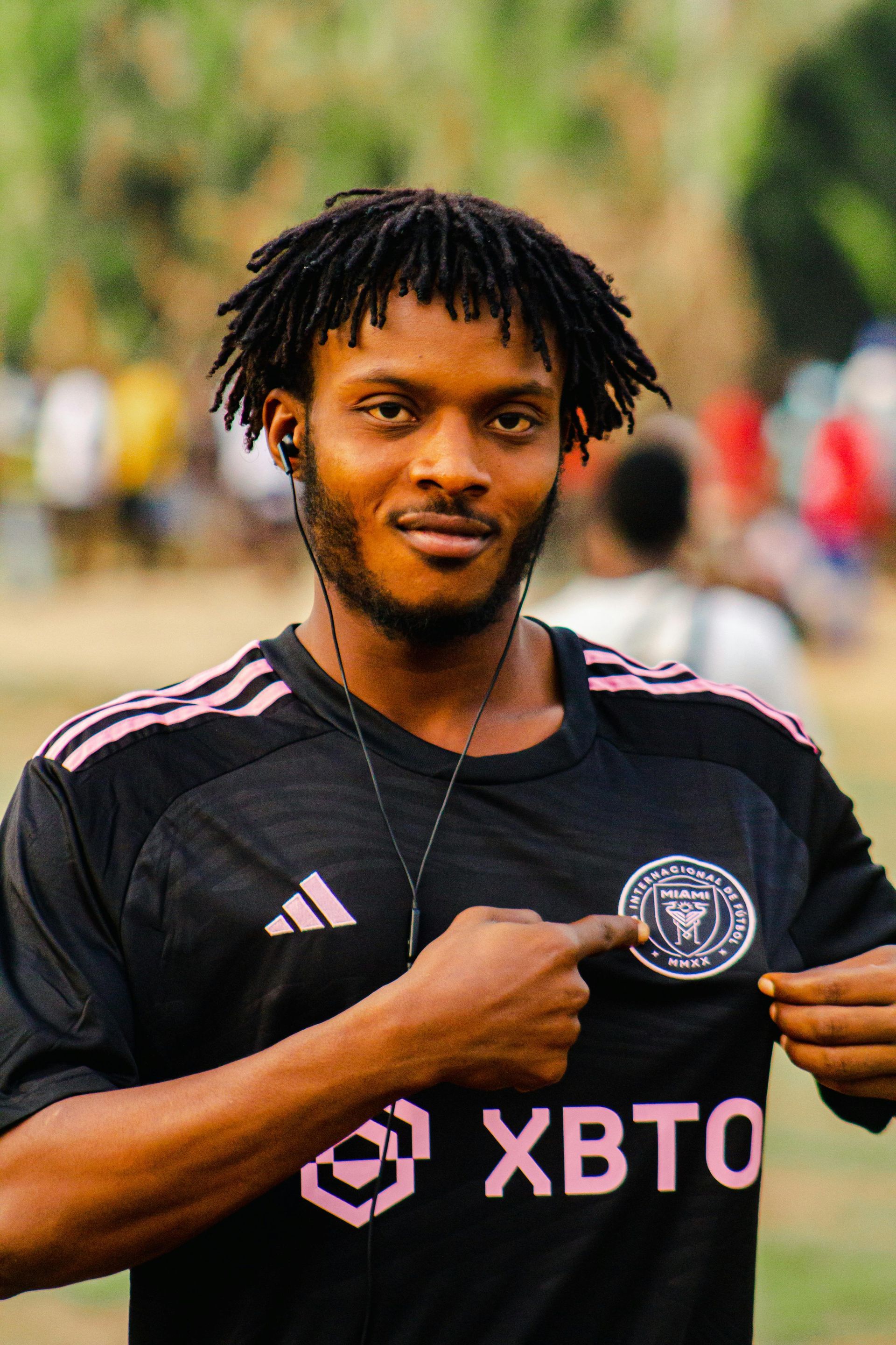A man wearing a black adidas shirt is pointing at a patch on his shirt.