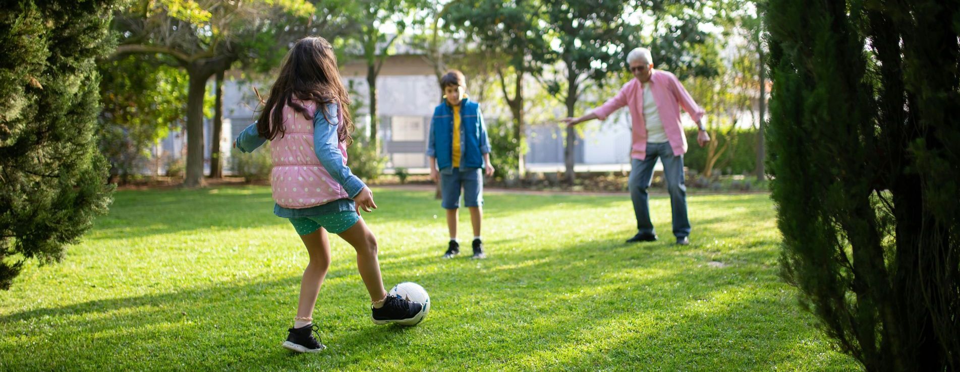 A girl is kicking a soccer ball in a park with her family.