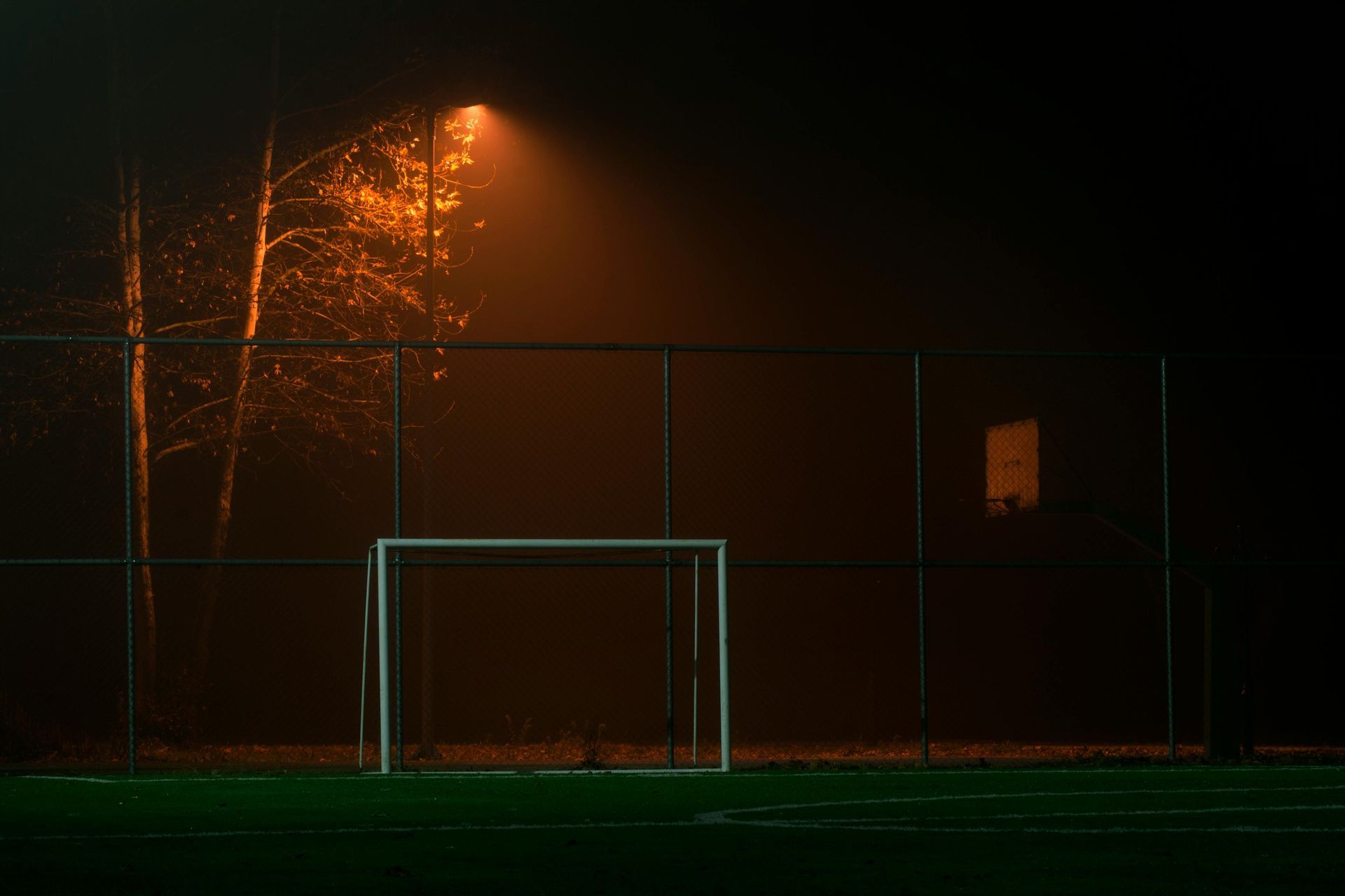 A soccer field at night with a goal and a fence.