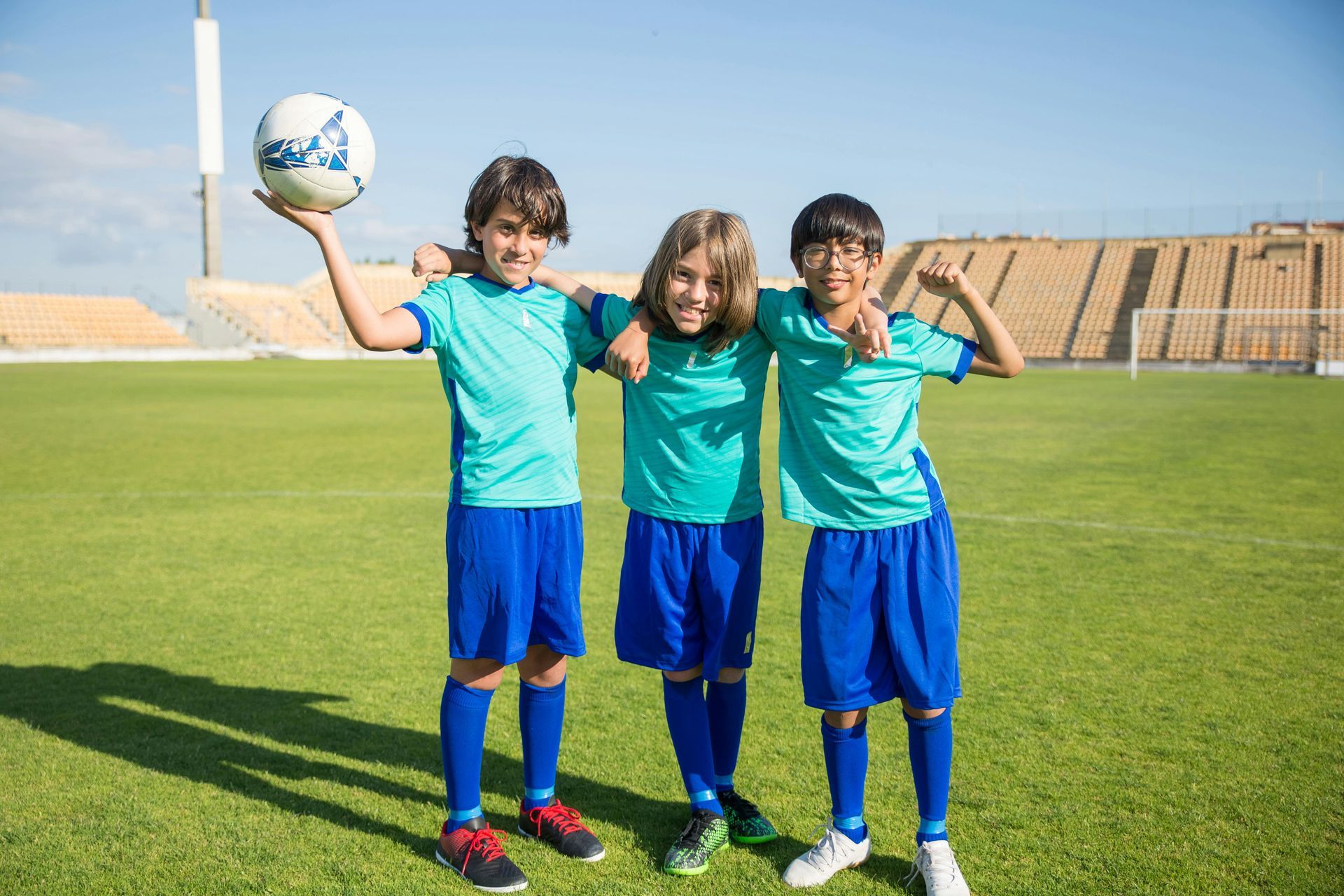 Three young boys are standing on a soccer field holding a soccer ball.