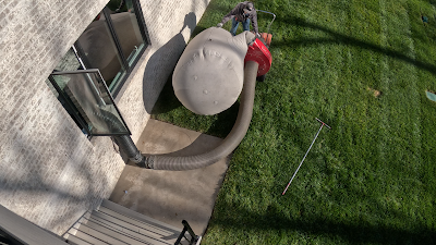 A person is using a vacuum cleaner to remove leaves from a lawn.
