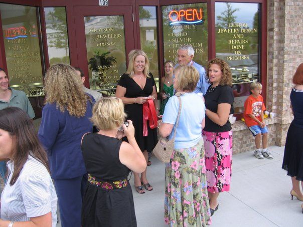A group of people are standing outside of a store with an open sign in the window