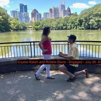 A man is proposing to a woman in front of a lake.