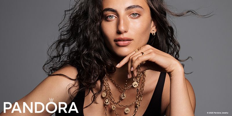 Woman with dark curly hair, wearing gold necklaces and earrings, for Pandora jewelry ad.