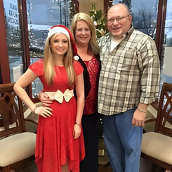 A woman in a santa hat is posing for a picture with her parents