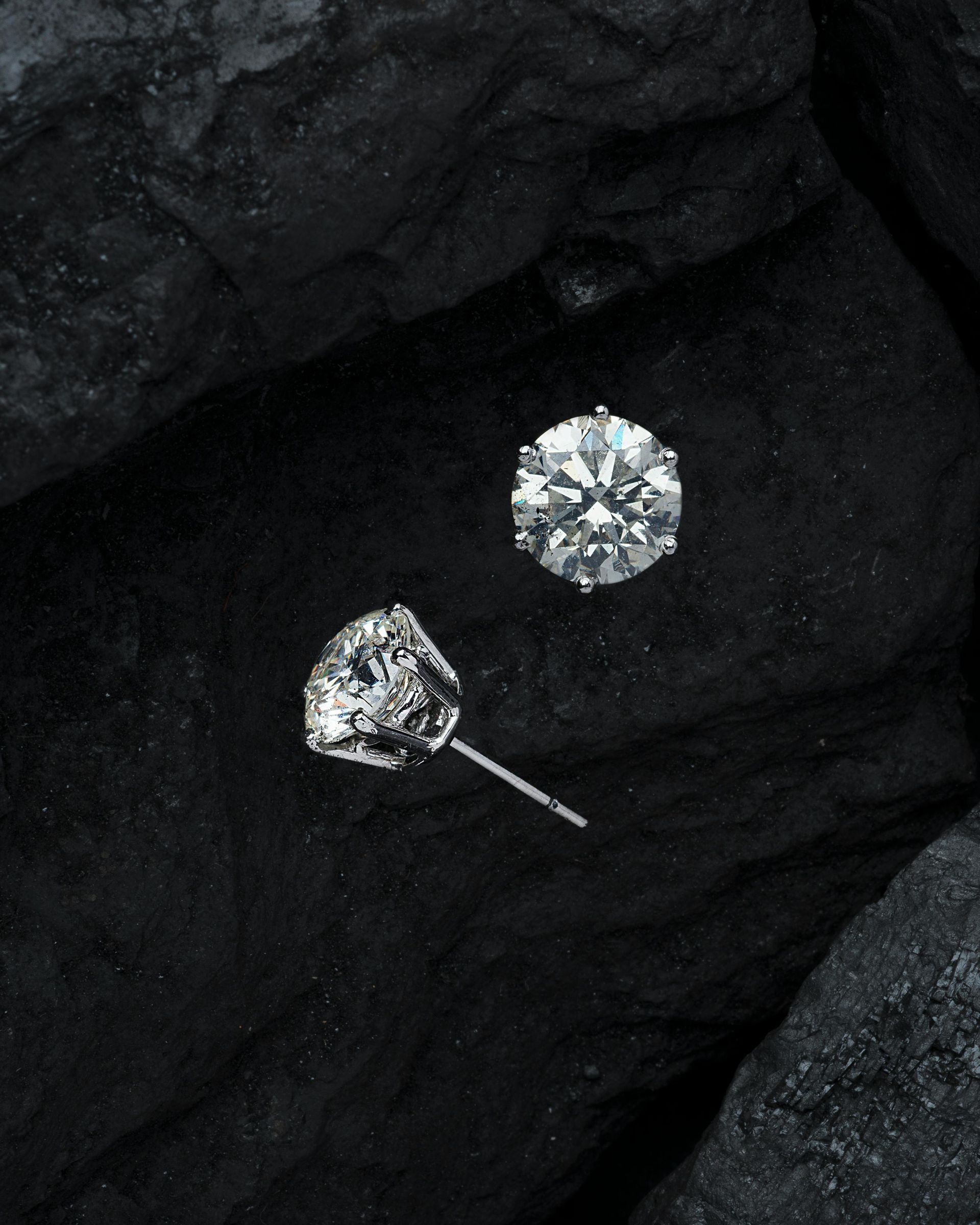 A pair of diamond stud earrings are sitting on a black surface.