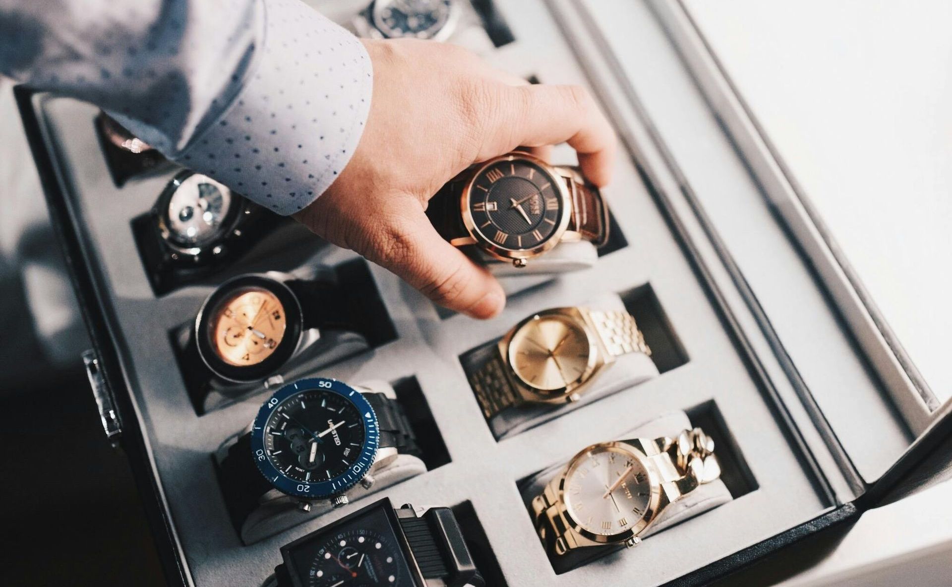 A person is taking a watch out of a box of watches.