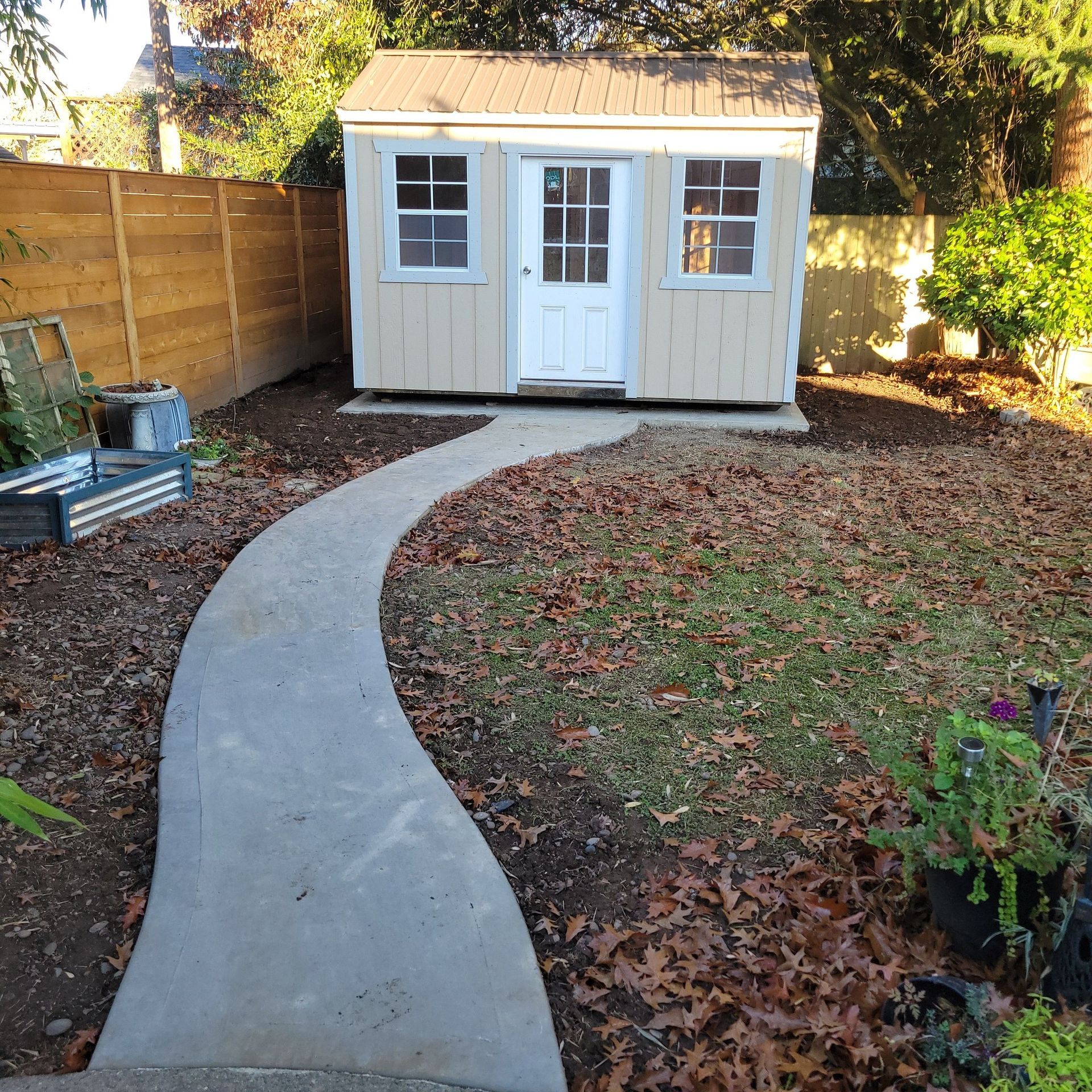 A shed in a backyard with a concrete walkway leading to it