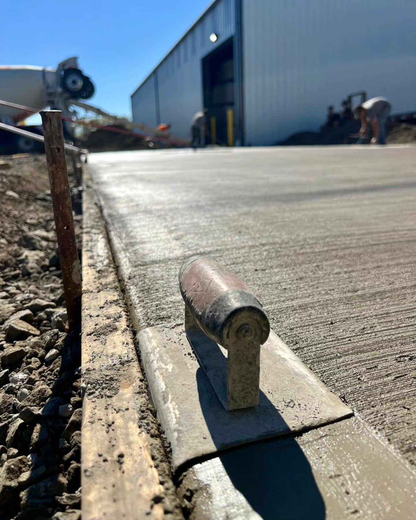 A trowel is laying concrete on a sidewalk in front of a building.