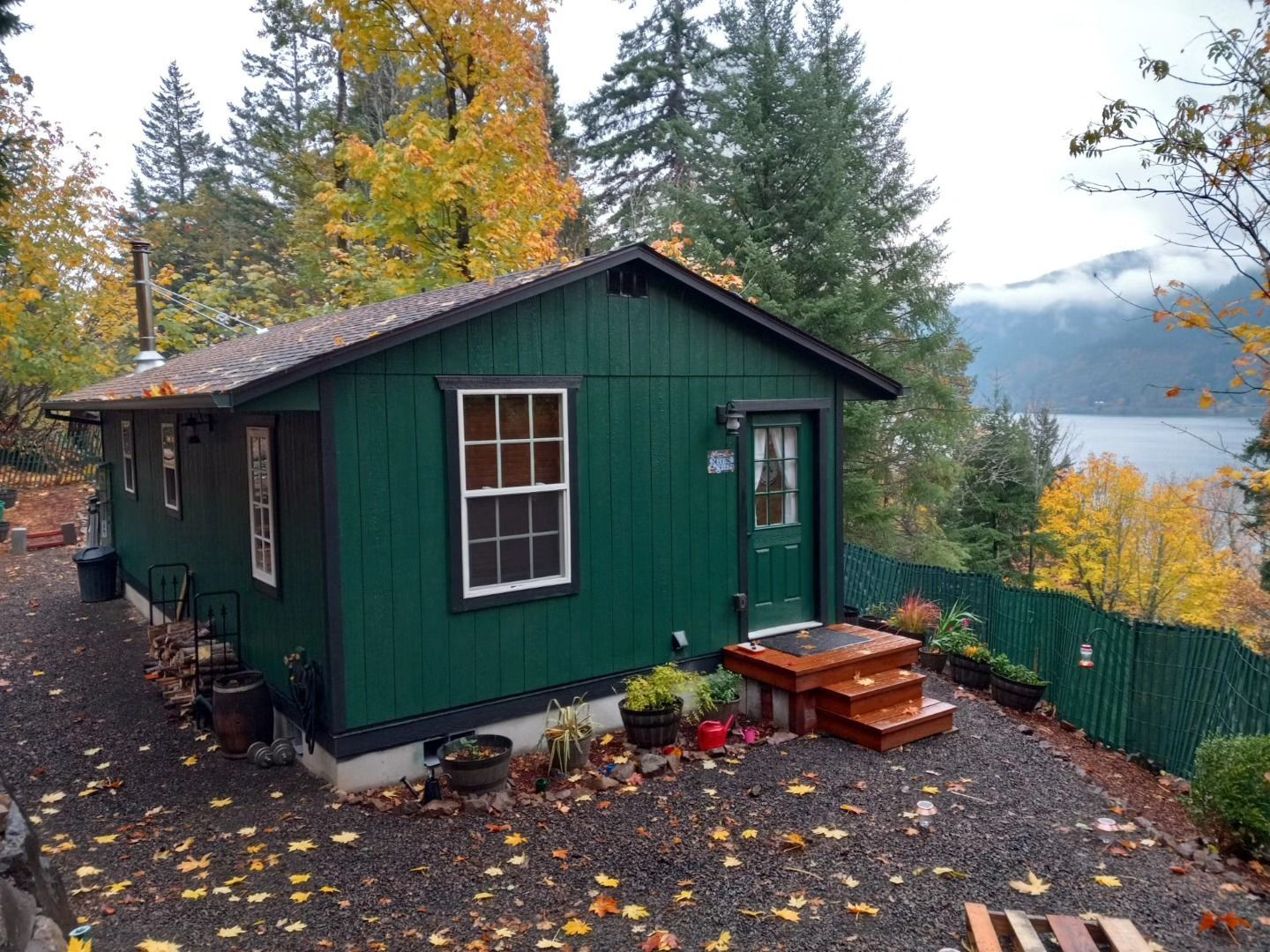 A small green house is sitting on top of a hill next to a lake.