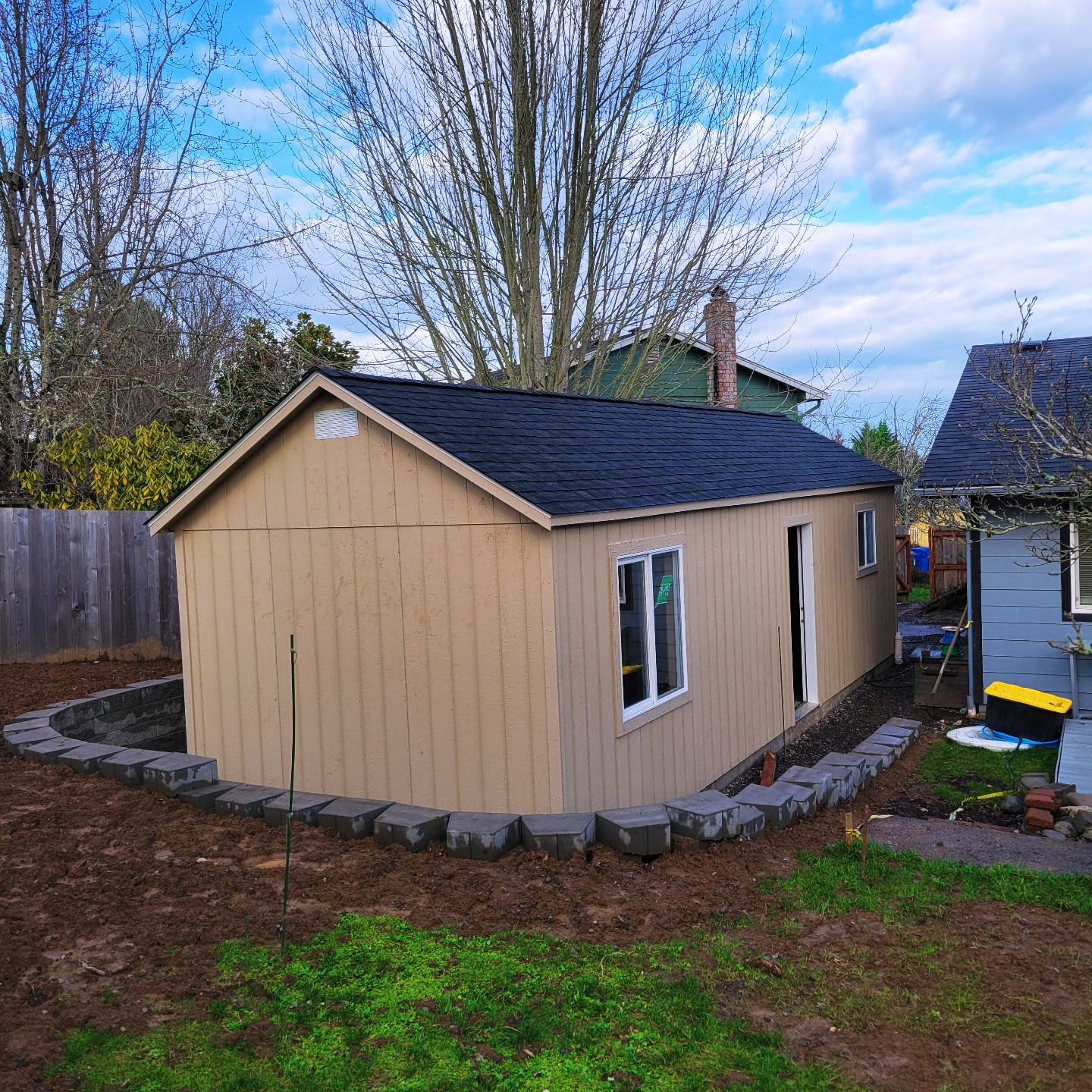 A small house with a black roof is in the backyard of a house.