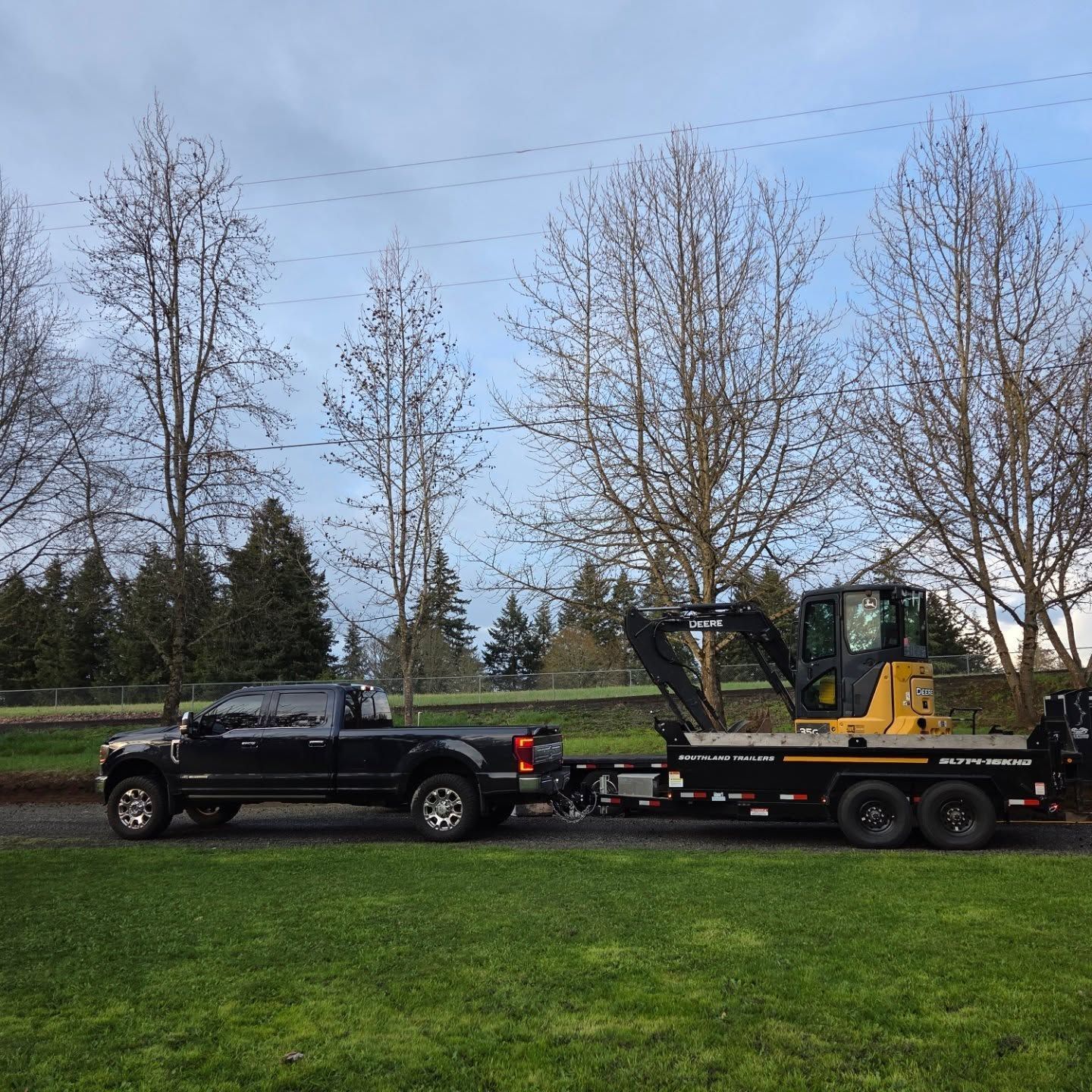 A black truck is towing a yellow excavator on a trailer
