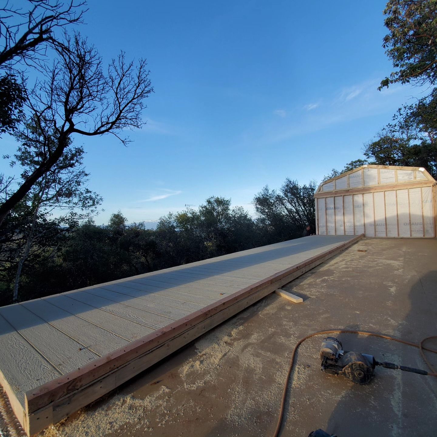 Construction site.  Flat roof with wooden framing and insulation against a backdrop of trees and a blue sky.
