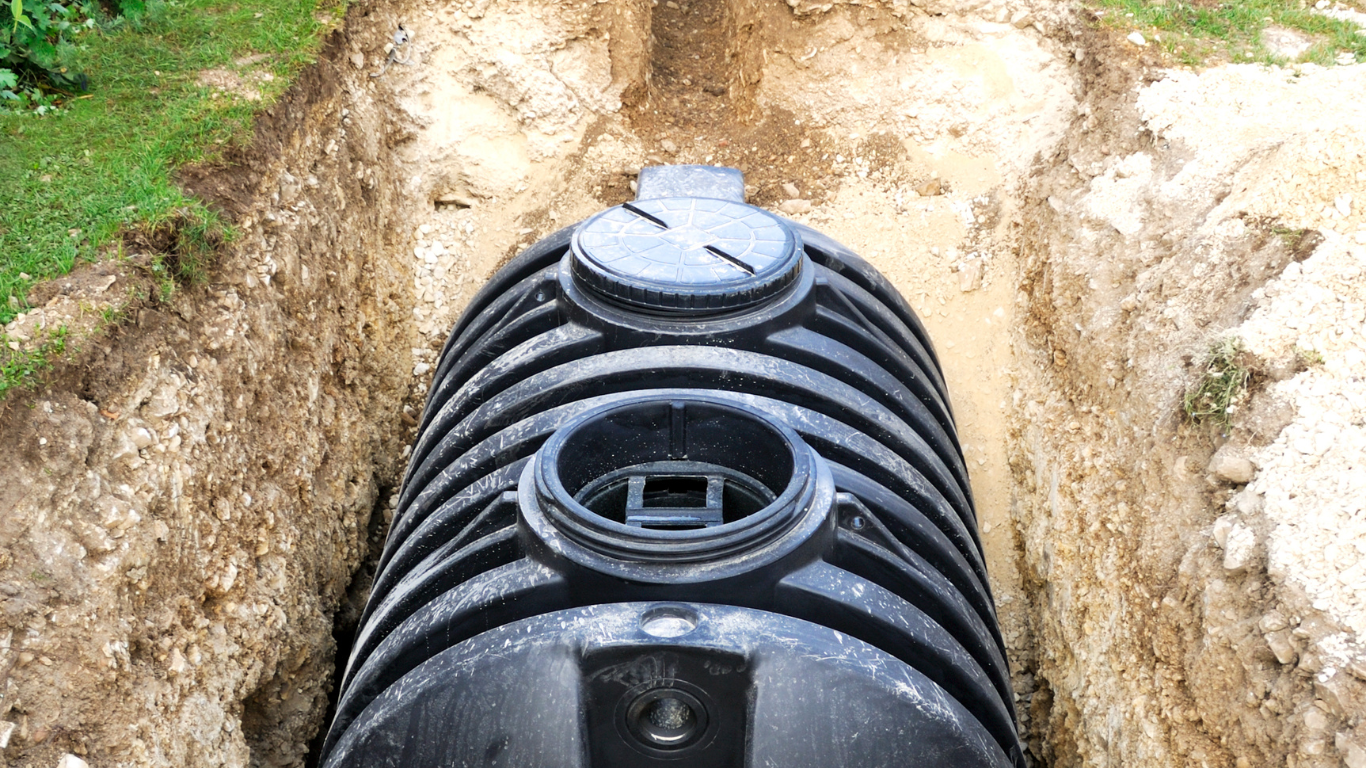A black plastic septic tank sits in an excavated trench in the ground.