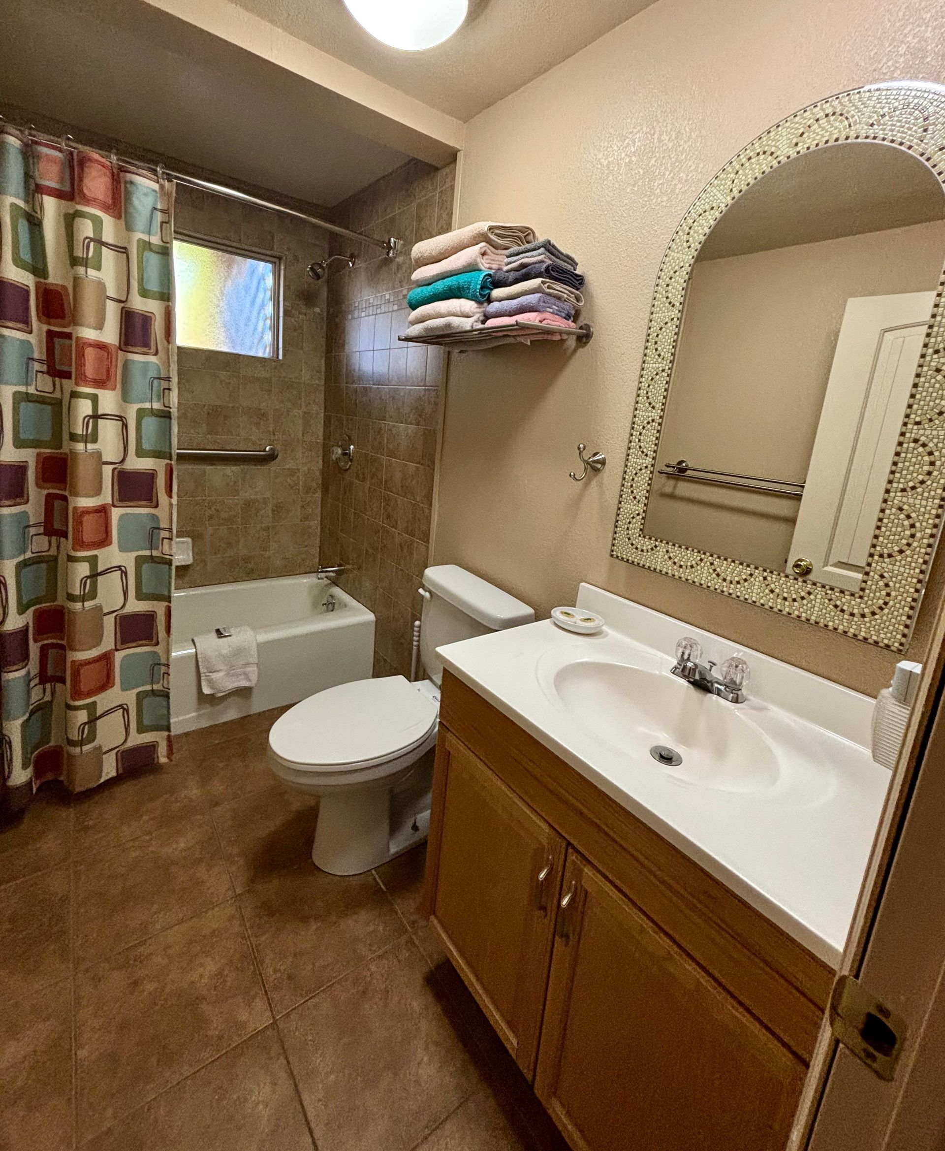 Bathroom with tub, toilet, vanity, and a stack of colorful towels on a shelf.