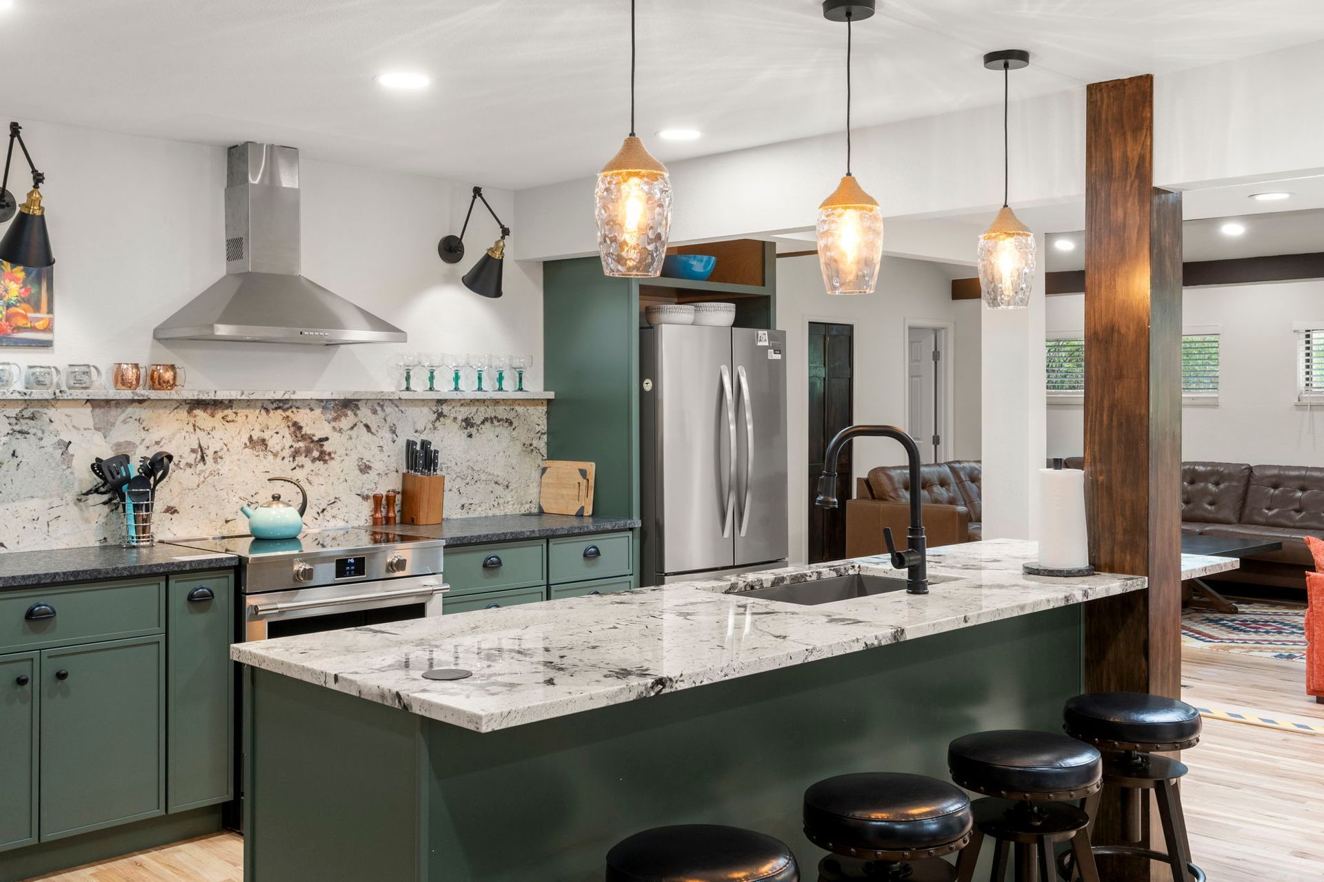 Green kitchen with granite countertops, stainless steel appliances, and hanging lights.