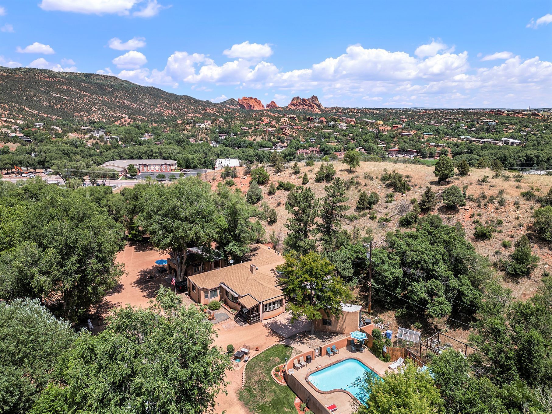 An aerial view of a house with a pool in the middle of a forest.
