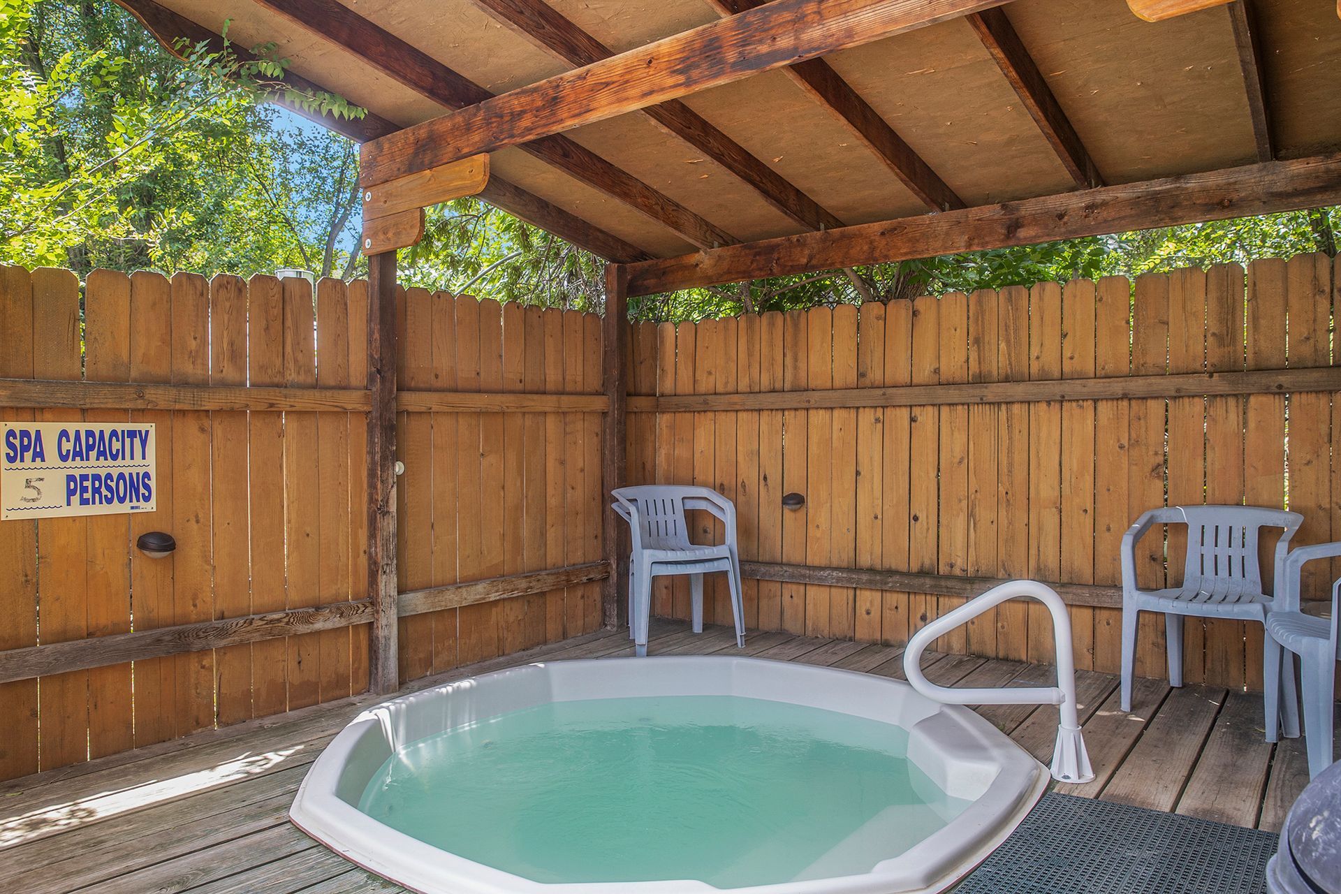 A hot tub is surrounded by a wooden fence and chairs.