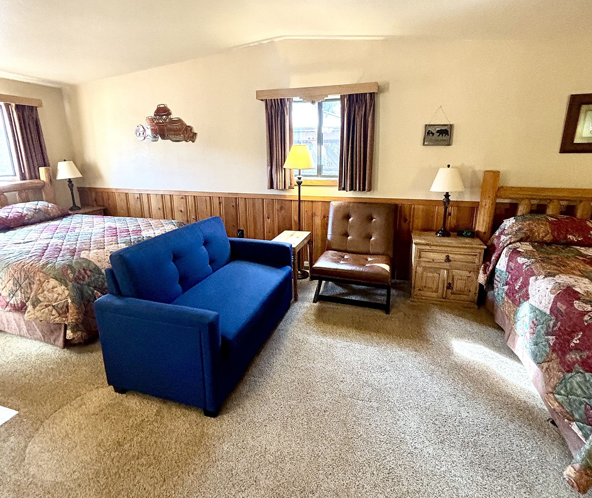 A hotel room with two beds, a blue couch, a chair, and two windows with curtains.