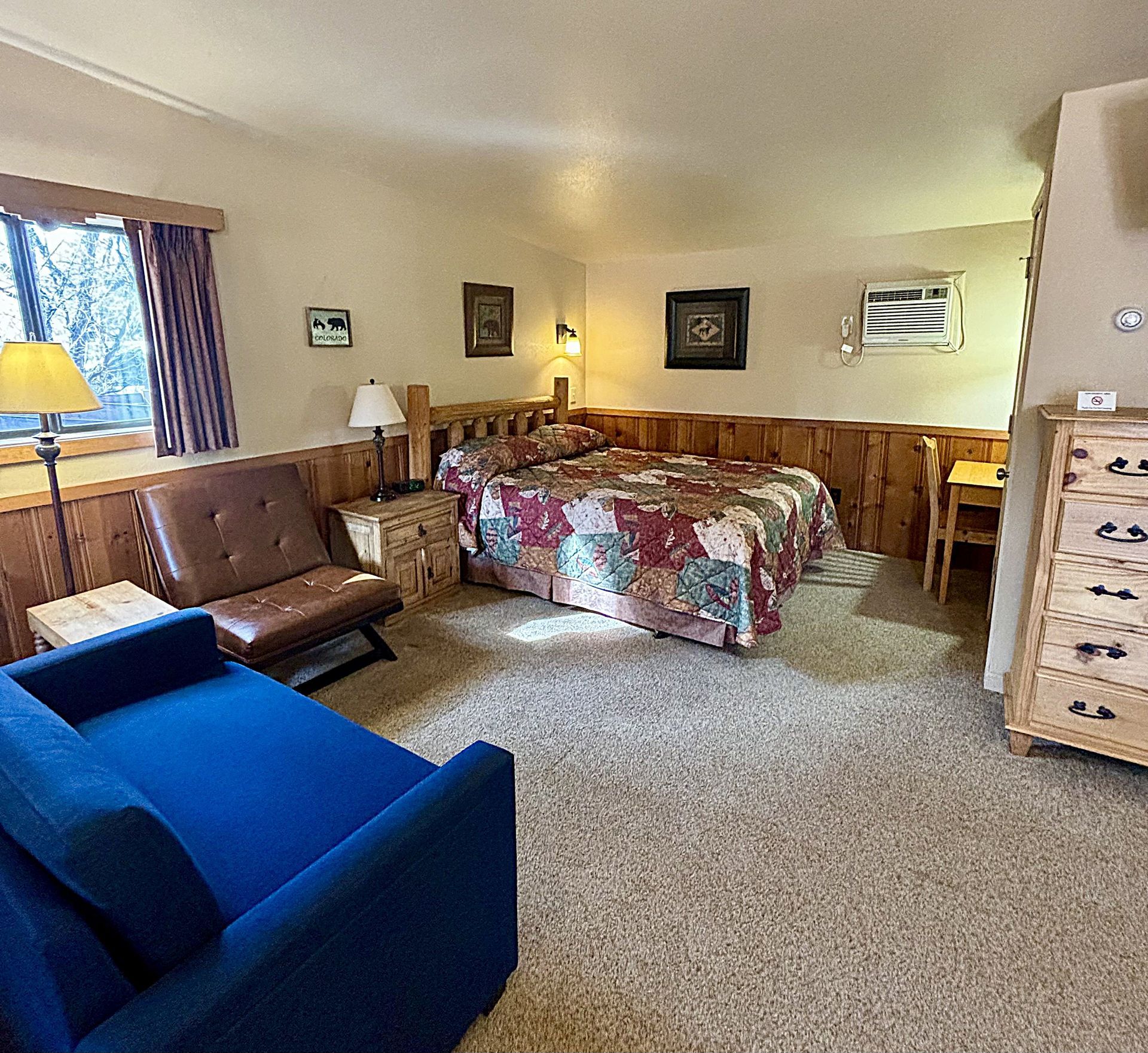Cozy motel room: bed with floral comforter, blue couch, wooden desk, and dresser.
