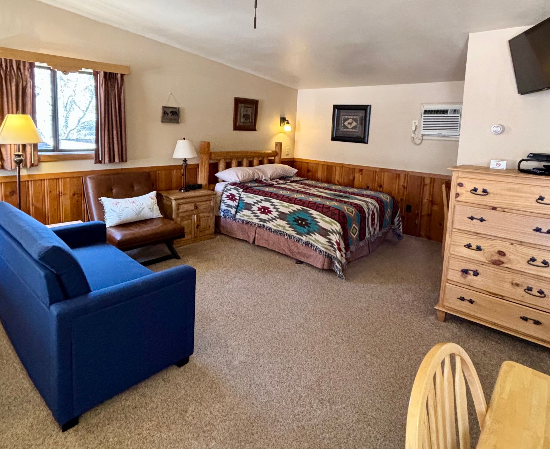 Cozy motel room: bed with colorful quilt, blue sofa, wooden dresser and accents.