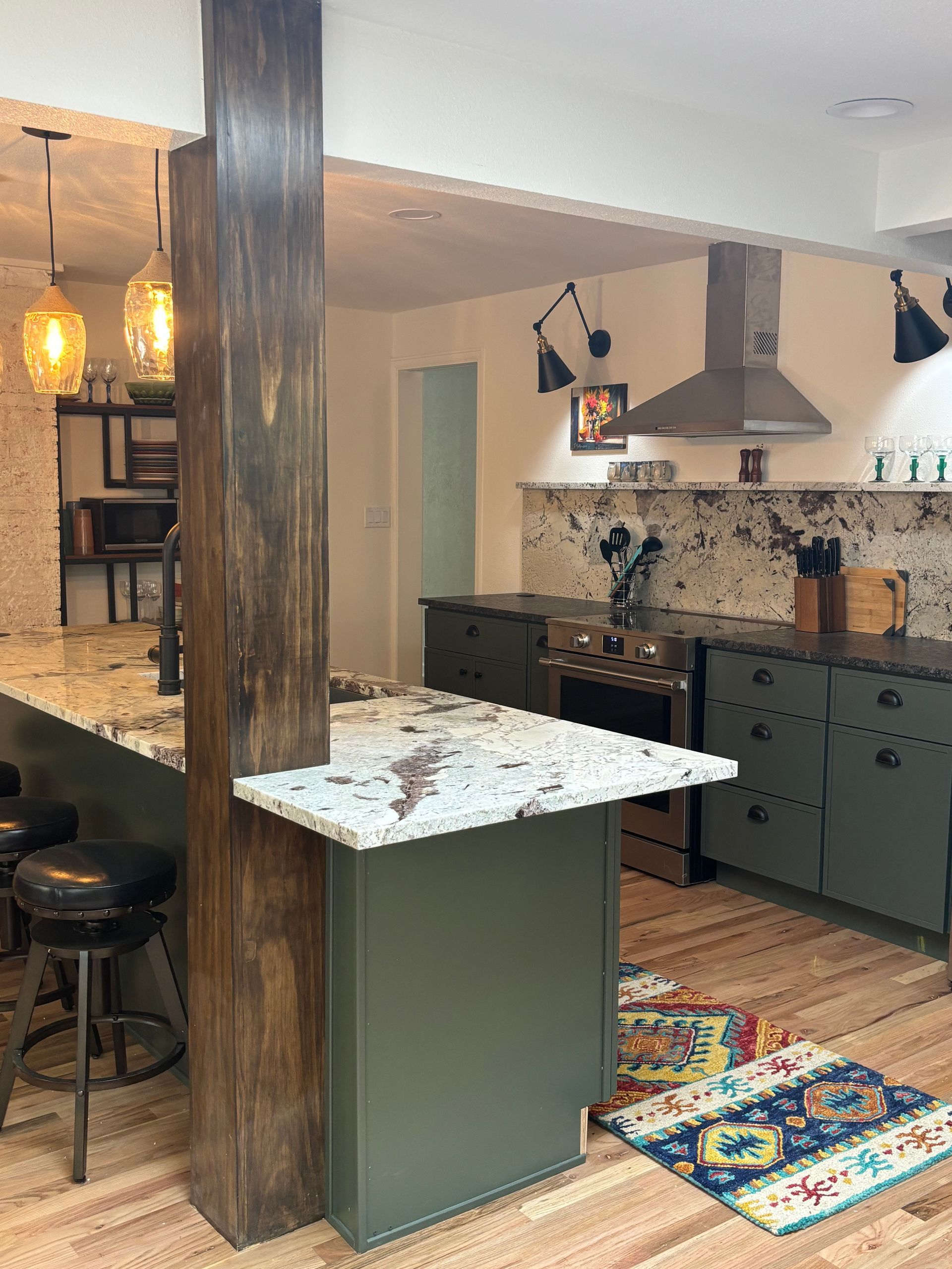 Kitchen with green cabinets, granite countertops, wooden column, and overhead lighting.