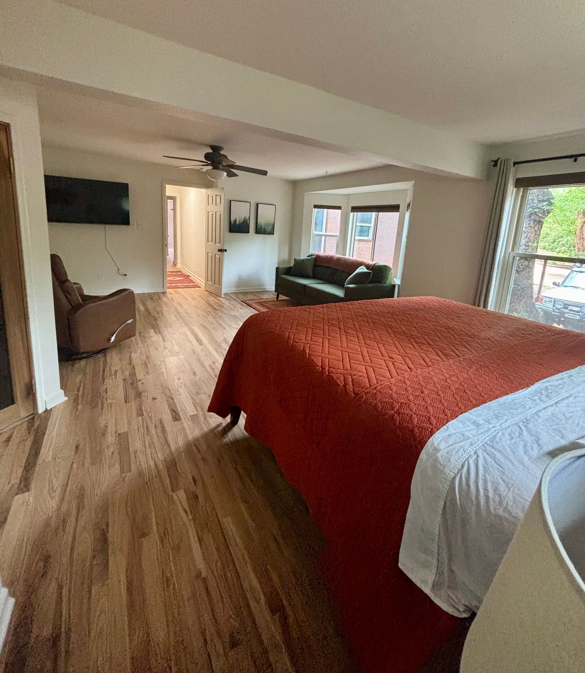 Bedroom with a large bed covered in red blanket, a green sofa, and wooden floors.