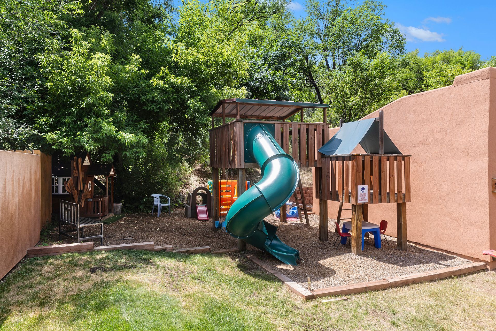 Playground with wooden structures, green slide, and gravel ground in a backyard.
