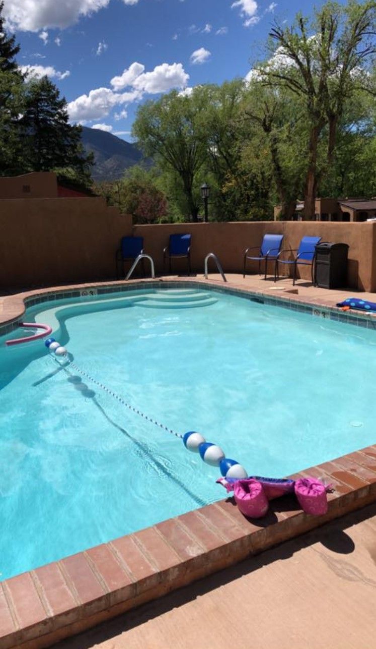 Swimming pool with blue water, brick border, and blue chairs. Trees and mountains in the background.