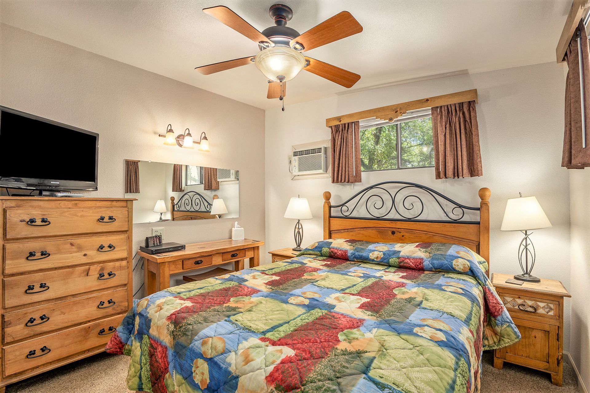 Bedroom with a bed, dresser, desk, and TV; decorated in warm colors, with a ceiling fan.