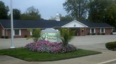 Fitzpatrick funeral home with a sign in front of it and flowers in front of it .