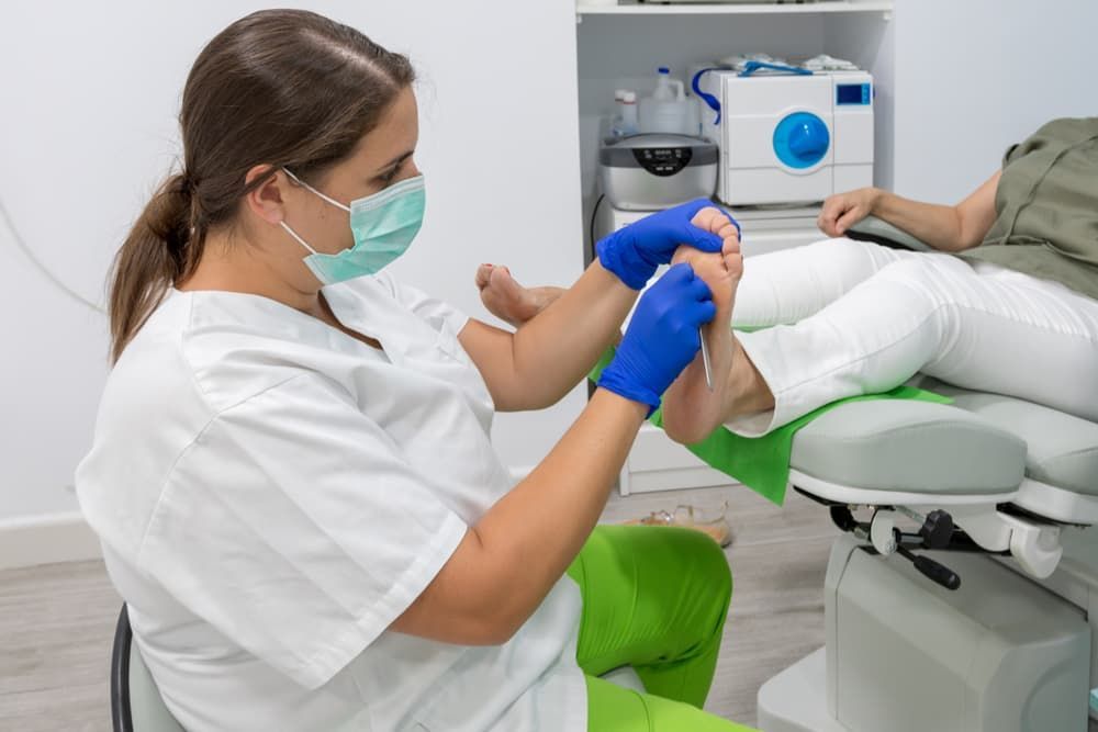 A woman is getting her feet examined by a podiatrist while wearing a mask. — Maitland Central Podiatry in Maitland NSW