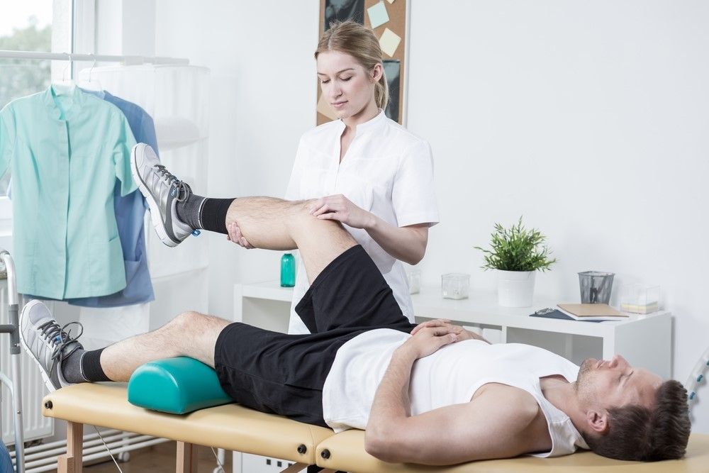 A Man is Laying on a Table While a Woman Stretches His Leg — Maitland Central Podiatry in Maitland NSW