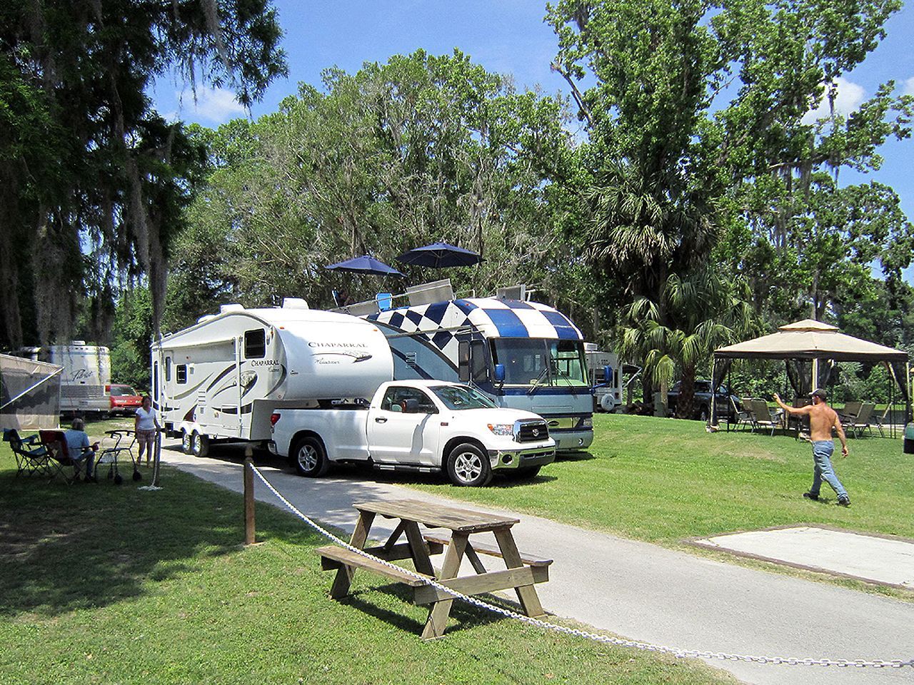a group of rvs are parked in a grassy area next to a picnic table .