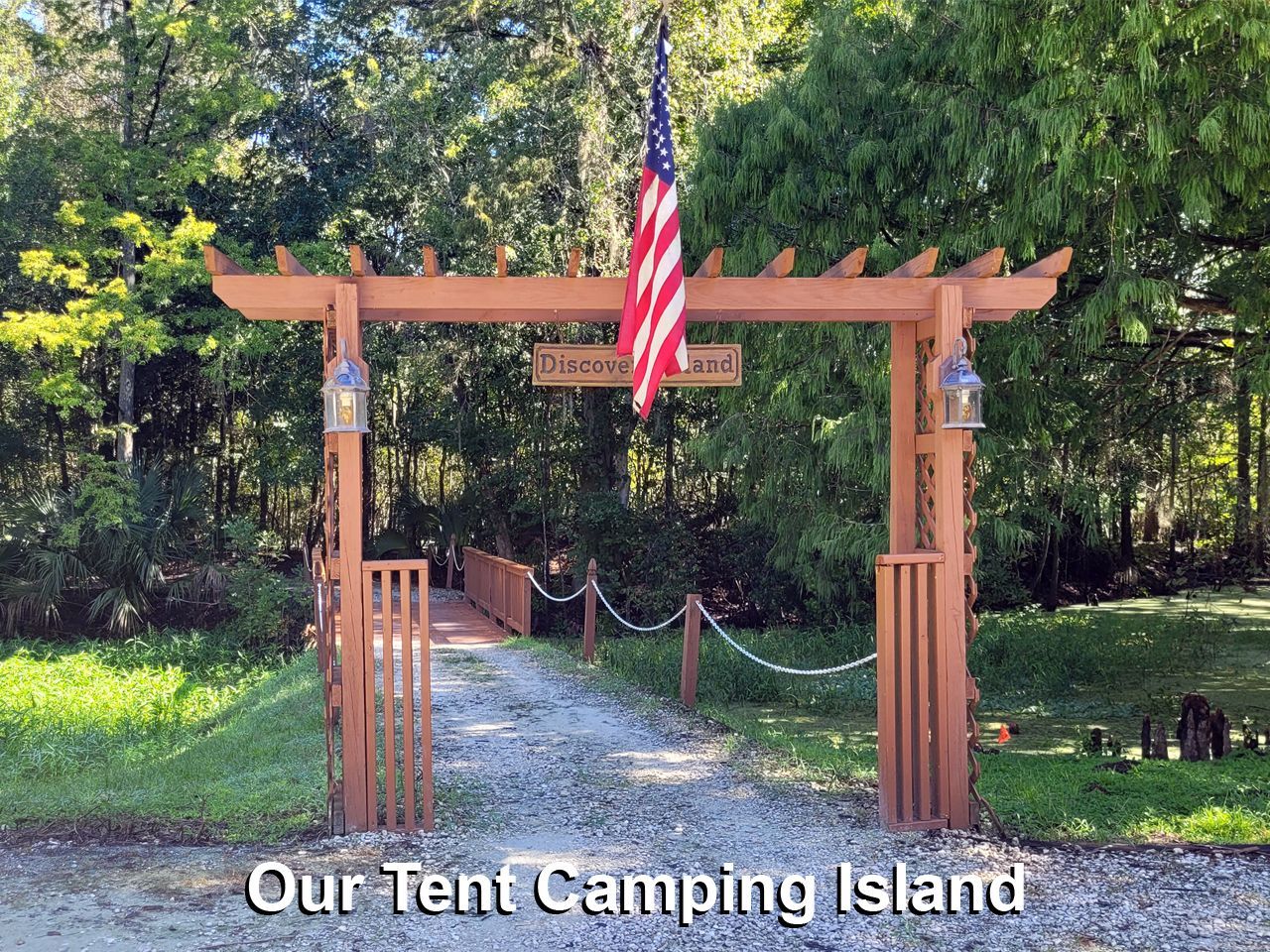 an american flag is flying over a wooden archway leading to our tent camping island .