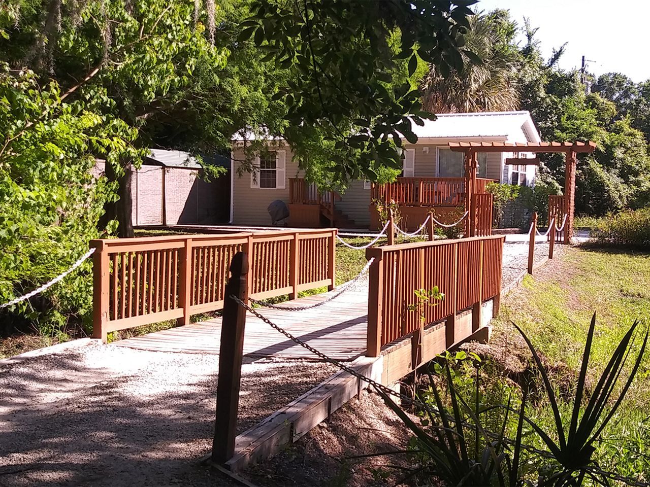 a wooden bridge over a dirt road leads to a house