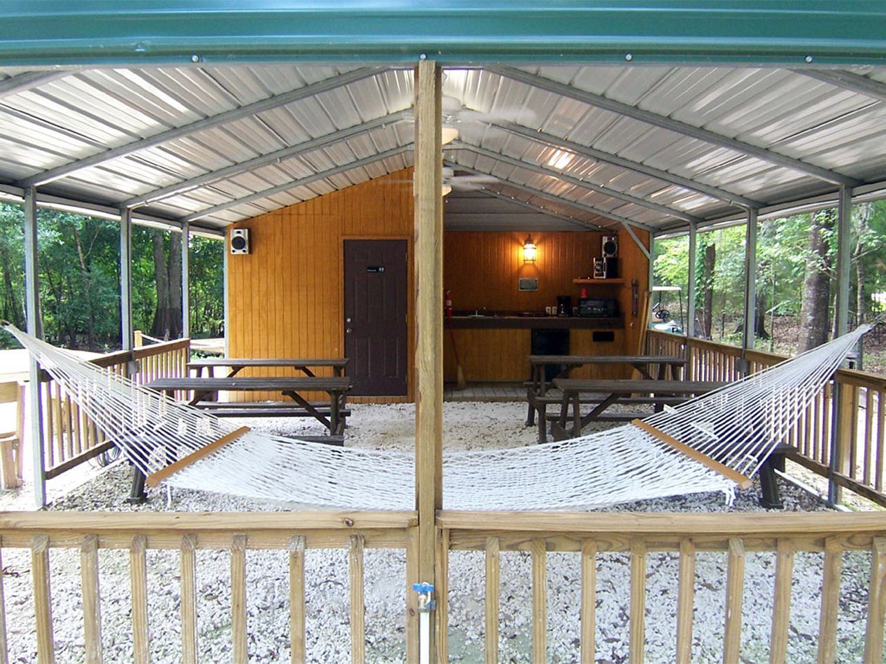 a covered porch with a hammock and picnic tables