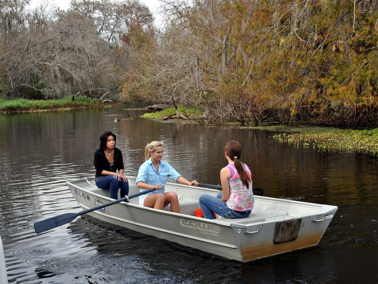 three women are rowing a boat on a river