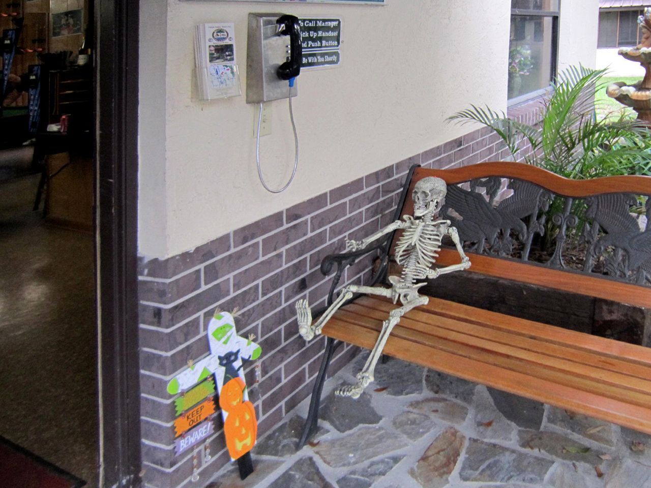 a skeleton is sitting on a bench next to a pay phone
