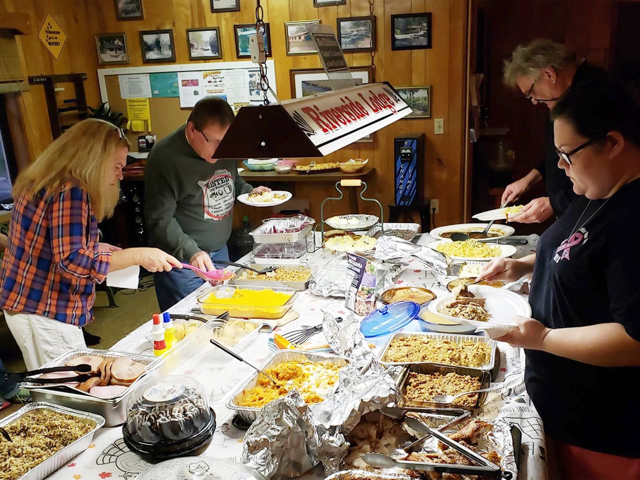 a group of people are standing around a long table filled with food .